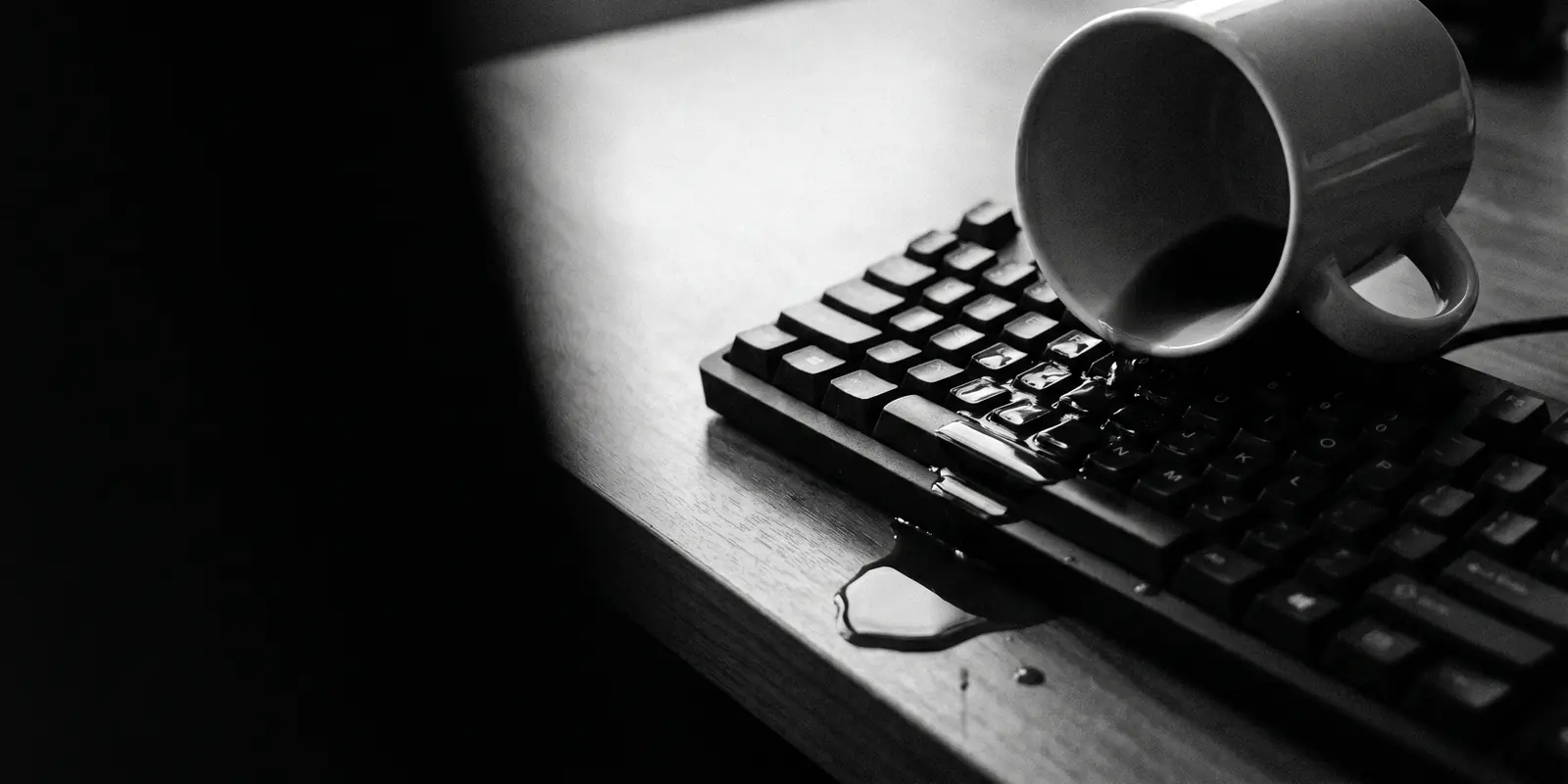 Een omgevallen koffiekopje ligt op een toetsenbord; koffie loopt over de toetsen en druppelt over de bureaurand — beeld voor de alledaagse storing.