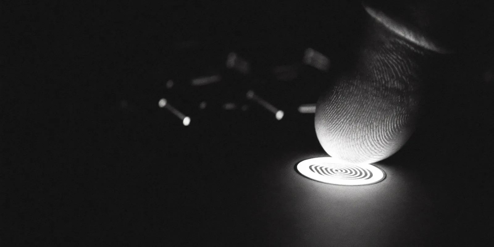 Een vingertop die een verlichte sensor aanraakt, in zwart-wit tegen een donkere achtergrond, als beeld voor inloggen met een passkey in plaats van een sms-code.